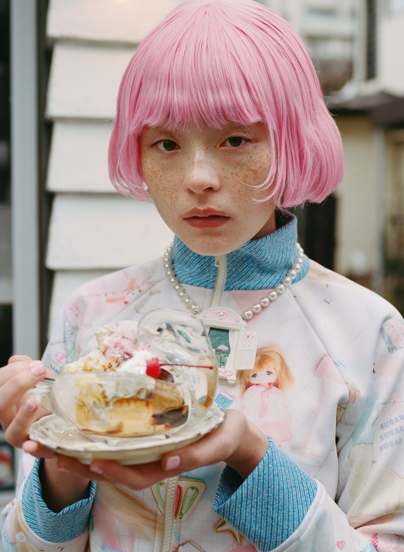 Model wearing a pink bob wig and printed zip-up jacket holding an ice cream sundae bowl