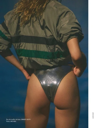 Model wearing a green track jacket and silver metallic swimsuit bottoms against a clear blue sky background.
