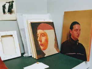 Oil painted portrait canvases, packaging materials, and blank stretcher frames arranged on a dark green studio surface.