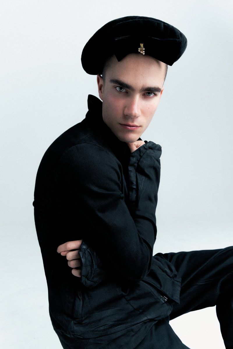 Male model in a black jacket and black beret posing against a white studio background.