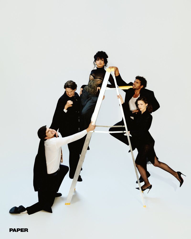 Five models dressed in black and white attire pose dynamically around and on a tall aluminum ladder against a white studio background.