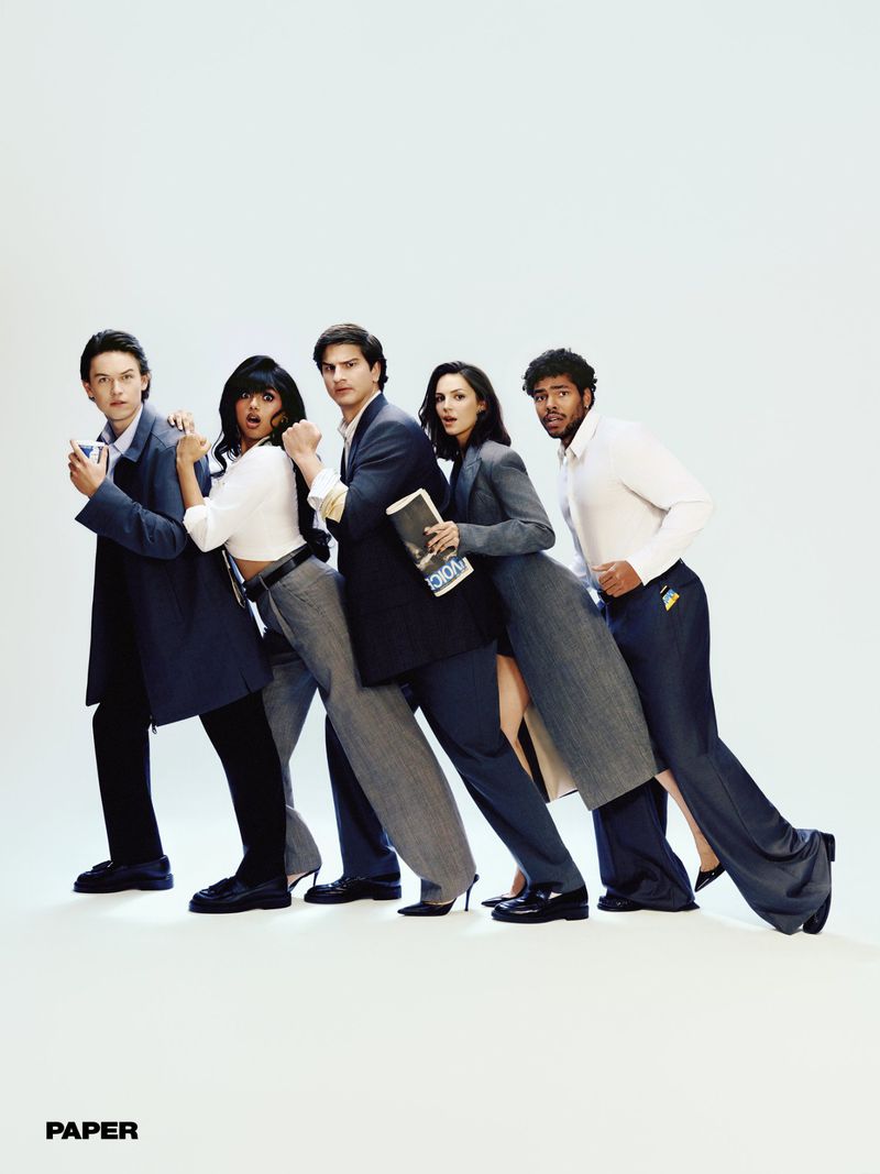 Five people in contemporary office attire posing in a diagonal leaning line against a plain white studio backdrop.