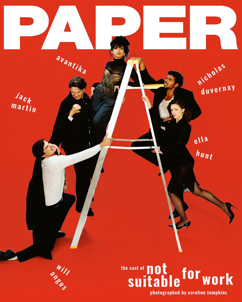 Cast of Not Suitable For Work posing playfully on a step ladder against a bright red studio backdrop for Paper Magazine.
