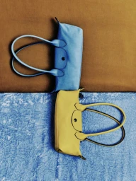 A blue leather handbag and a yellow leather handbag laid flat on a split brown and blue textured fabric backdrop.