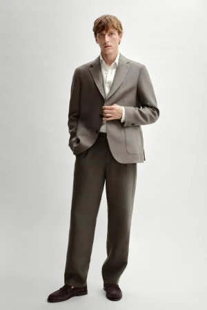 Full-length portrait of a male model wearing a grey suit jacket, trousers, white shirt, and dark loafers against a white backdrop