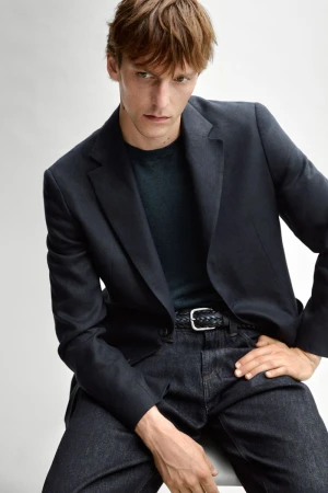 Model Quentin Demeester wearing a dark tailored blazer, crewneck top, braided belt, and dark jeans against a white seamless backdrop.