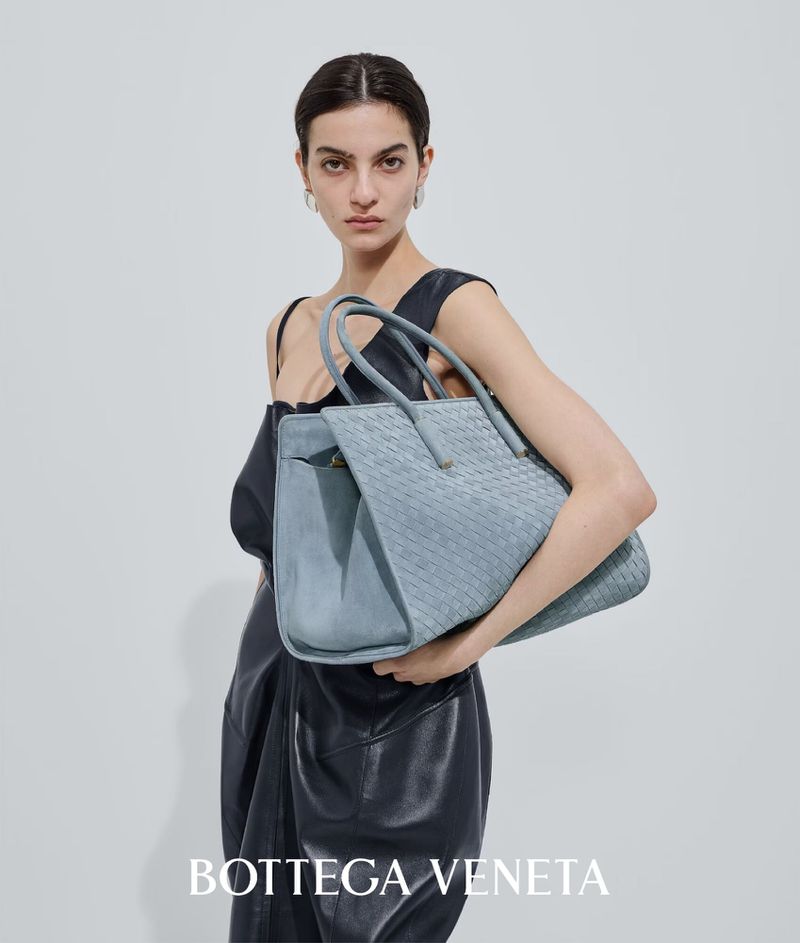 Anna Kirjuskina holds a light blue woven leather Bottega Veneta tote bag against a neutral studio background.