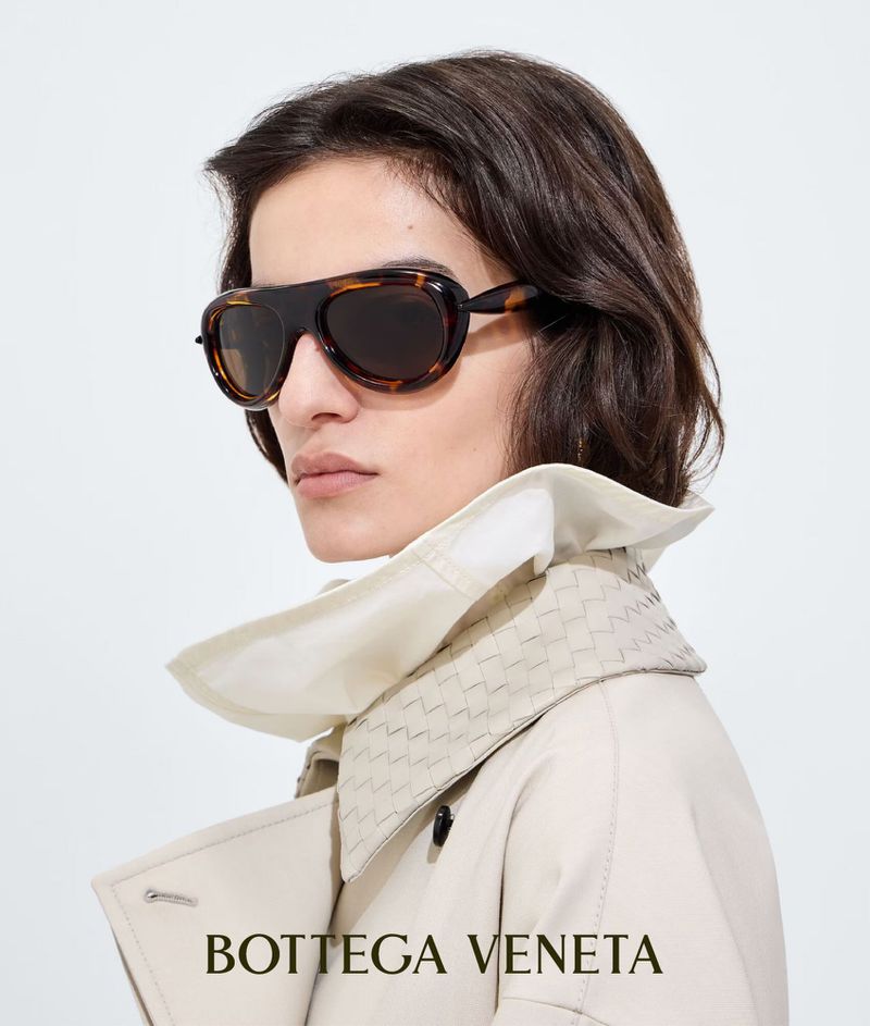 Anna Kirjuskina wearing tortoiseshell sunglasses and an off-white trench coat with woven collar against a white background.