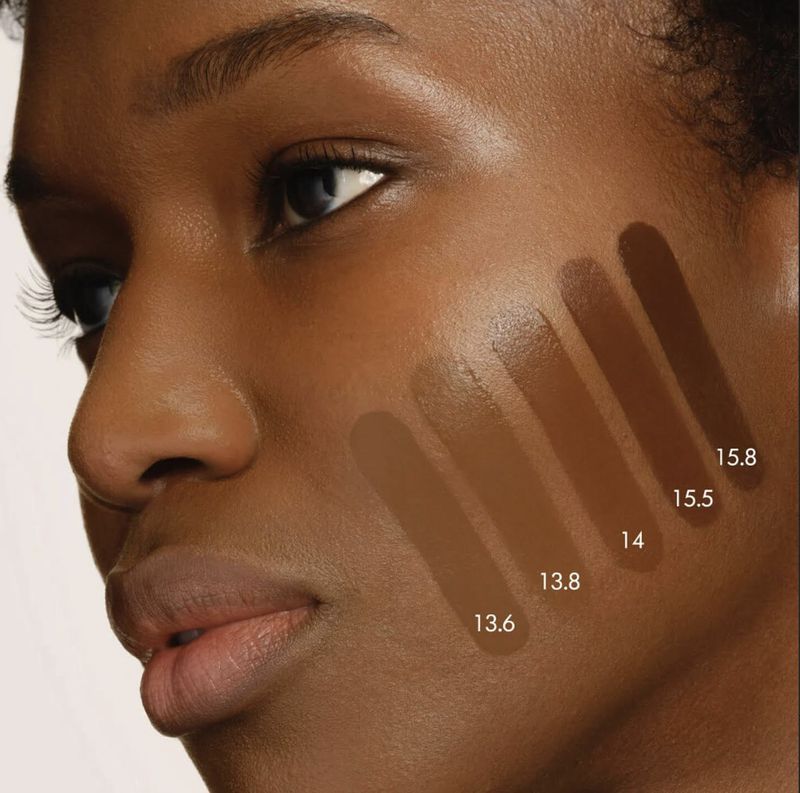 Close-up of model Tiah Beye's cheek showing five liquid foundation shade swatches labeled with numbers for Armani Beauty.