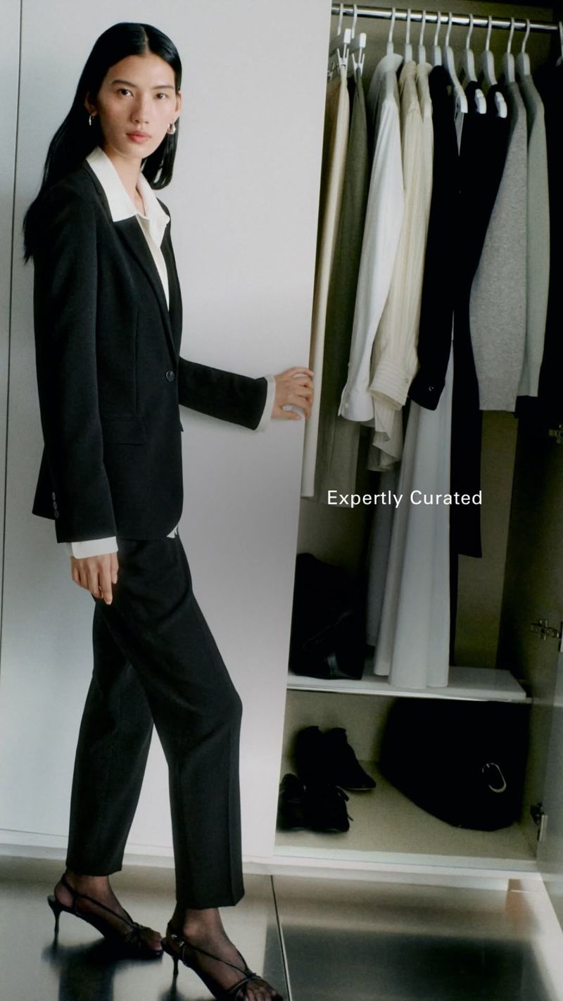 Model Jiayun Xie wearing a black suit standing beside an open white wardrobe filled with hung clothing.