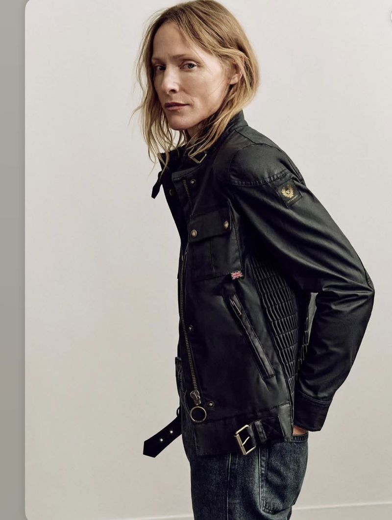 Model Lindsay Sullivan wearing a black Belstaff waxed motorcycle jacket and jeans against a neutral studio backdrop.