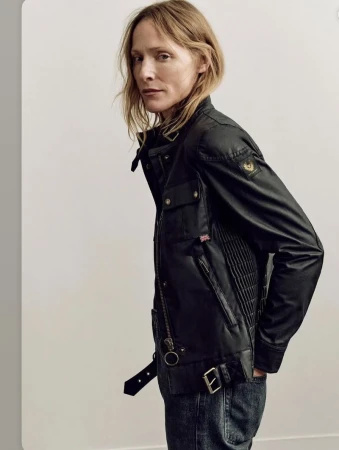 Model Lindsay Sullivan wearing a black Belstaff waxed motorcycle jacket and jeans against a neutral studio backdrop.