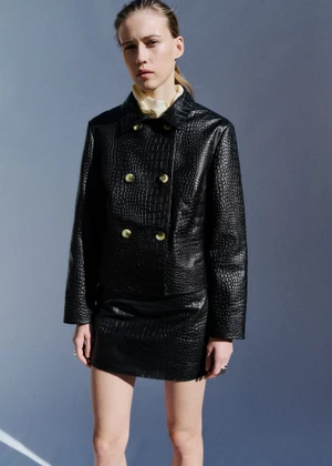 Model Liva Been wearing a black crocodile-embossed jacket and matching mini skirt against a cool grey studio backdrop.