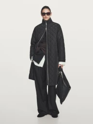 Model Aleyna Fitzgerald wearing a black quilted coat, wide-leg trousers, and sunglasses against a studio backdrop