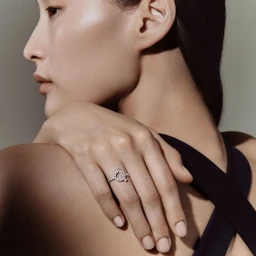 East Asian model in profile resting a hand adorned with a diamond ring on her shoulder against a neutral studio backdrop.