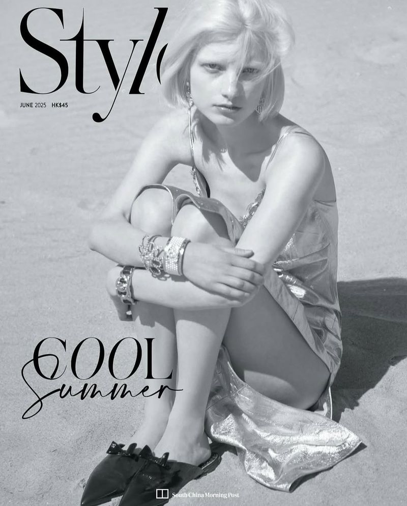 Black and white fashion editorial featuring a blonde model in a metallic dress sitting on a sandy beach with jewelry.