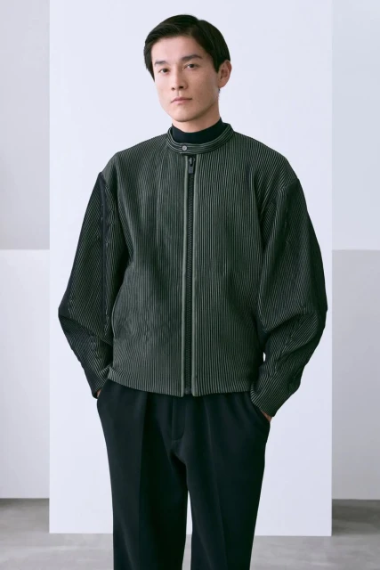A stylish Asian man in a black turtleneck and striped jacket poses confidently against a white background in a studio setting.