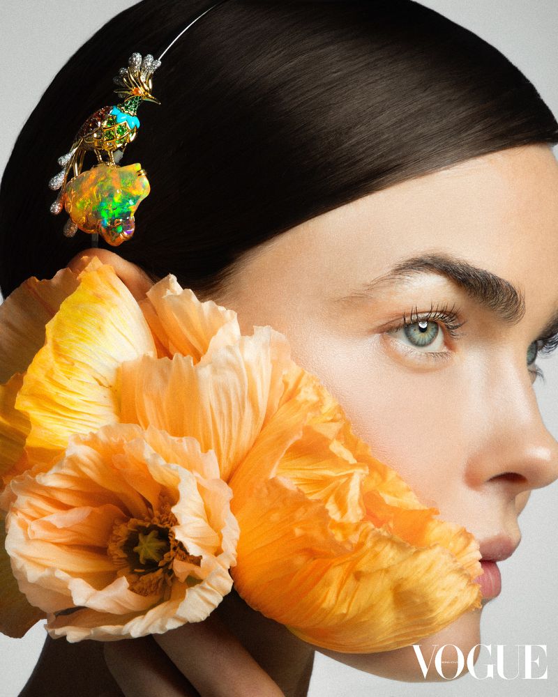 Model Bambi Northwood Blyth holding yellow poppy flowers near her face while wearing an ornate jeweled bird brooch in her hair.