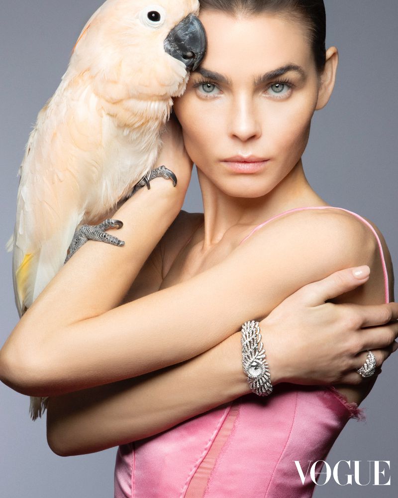 Bambi Northwood Blyth holding a cockatoo on her arm while wearing a pink satin top and diamond watch against a grey background.