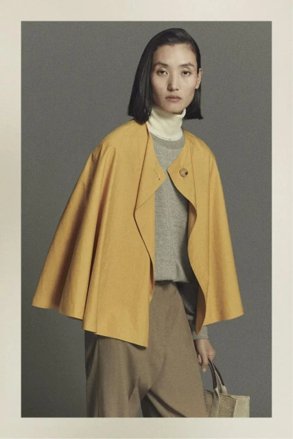 Asian woman in yellow open coat, gray sweater, and khaki pants with a tote bag, studio shot for fashion or editorial use.
