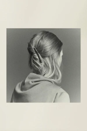 Blond woman with a twist hairstyle, wearing a top, shot from the back. Focus on the hair accessory, against a grey backdrop.