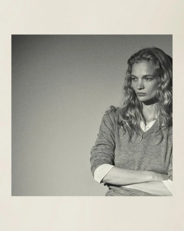 Portrait of a blonde woman in a grey sweater with crossed arms. Studio-style with a minimalist background and neutral colour palette.