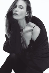 Monochrome portrait of model Behati Prinsloo wearing an oversized black coat and delicate choker necklace against a white background.