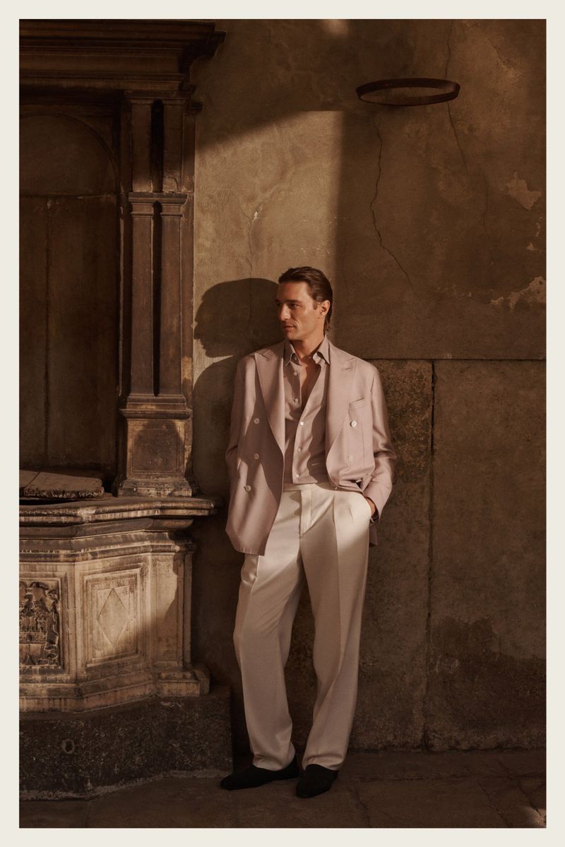 A stylish adult male stands in a suit near an archway with neutral tones and shadows, offering a timeless and sophisticated image.