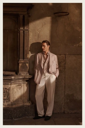A stylish adult male stands in a suit near an archway with neutral tones and shadows, offering a timeless and sophisticated image.