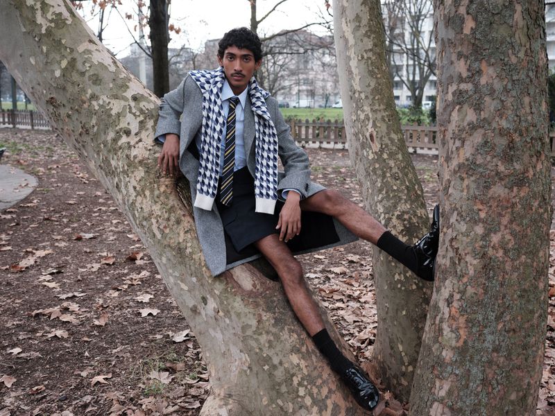 Model Viknes Waren perched in the crook of a large sycamore tree wearing a grey wool coat, houndstooth scarf, and black tailored shorts.