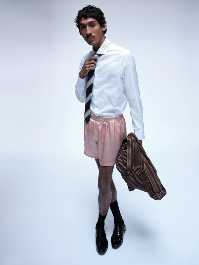 Model Viknes Waren wearing a white dress shirt, striped tie, and pink satin boxers against a pale studio backdrop.