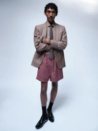 Model Viknes Waren in a taupe tailored blazer, tie, and pink striped boxer shorts against a light grey studio background.