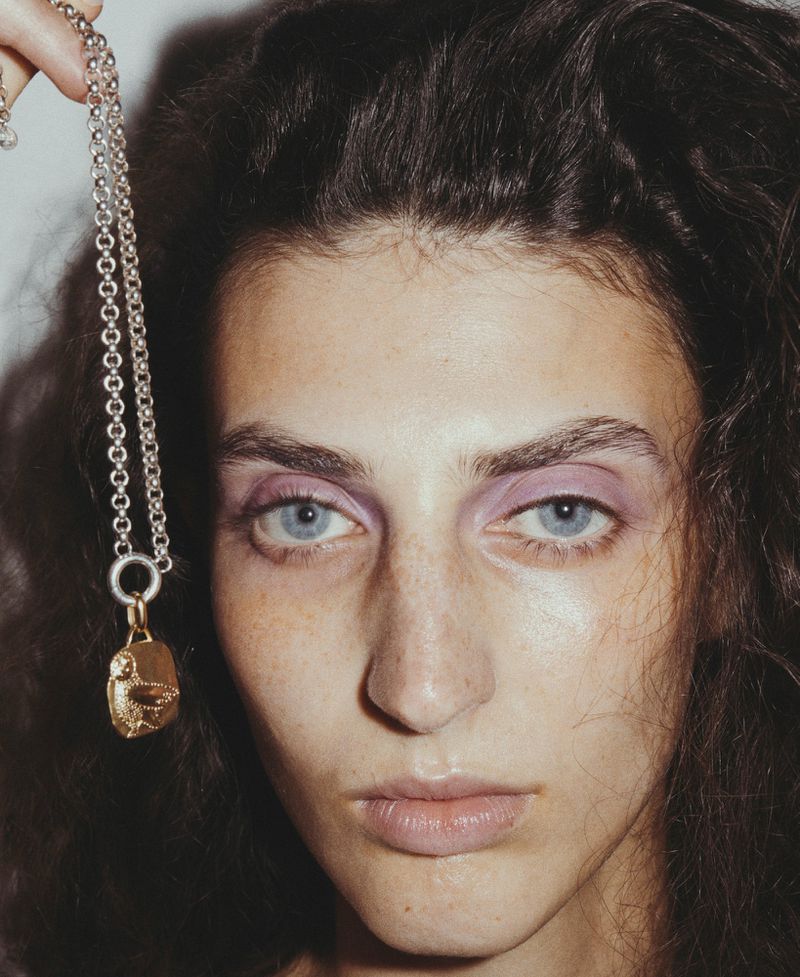 Close-up portrait of Anna Papini beside a dangling silver chain featuring a gold owl medallion pendant.