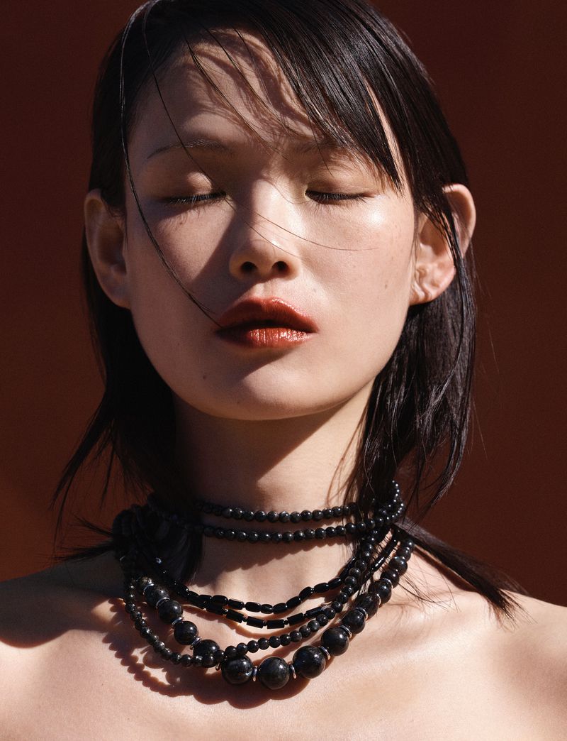 Close-up portrait of model Xie Chaoyu with eyes closed wearing layered black bead necklaces for Vogue Thailand