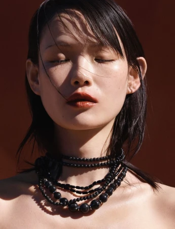 Close-up portrait of model Xie Chaoyu with eyes closed wearing layered black bead necklaces for Vogue Thailand