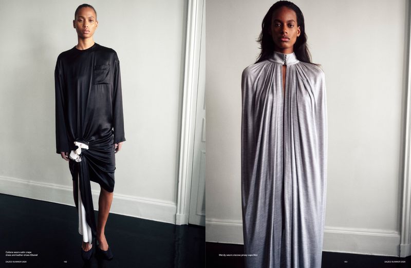 Two fashion models posing side by side in a minimalist interior with white walls and a dark glossy floor.