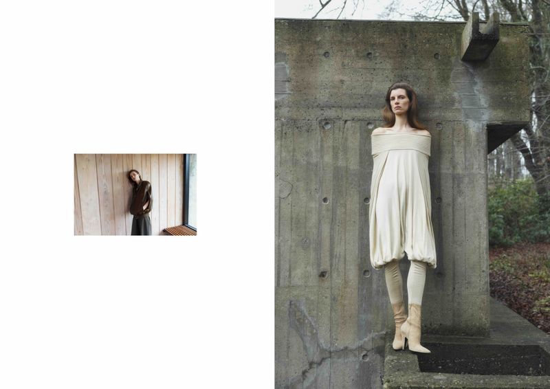 Model Luca Gajdus poses outdoors in a cream off-the-shoulder draped tunic and leggings against a weathered concrete structure.