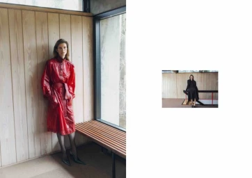 Model Luca Gajdus wearing a belted glossy red trench coat standing beside a slatted wood bench and window.