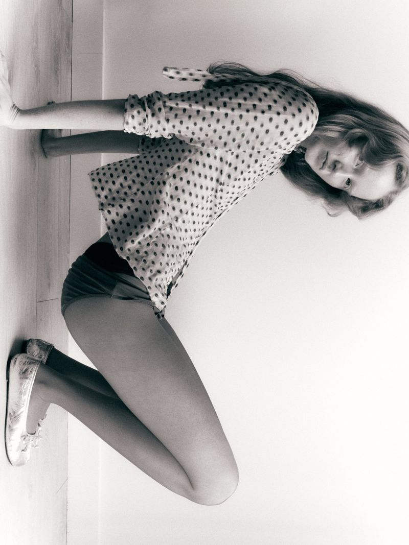 Model Lucy Arbuthnott crouching in a polka dot blouse and patterned ballet flats against a plain studio background.