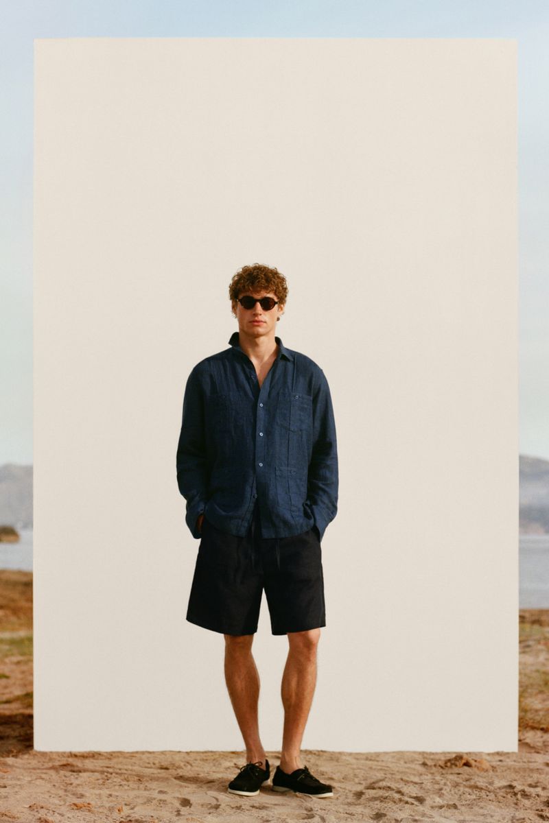 Model Valentin Humbroich posing in a navy overshirt, black shorts, and sunglasses against a freestanding backdrop.