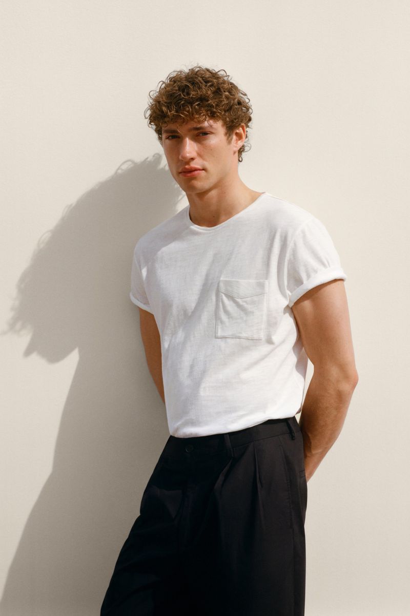 Model Valentin Humbroich wearing a white t-shirt and black trousers against a plain seamless studio background