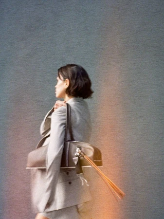 Model Noah Ramos carrying a brown leather shoulder bag with long fringe tassels, wearing a grey tailored blazer.