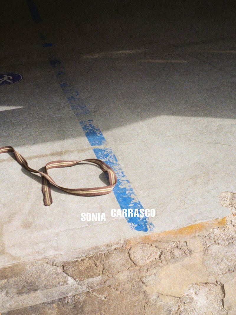 Striped fabric belt lying looped on concrete ground next to a weathered blue painted line in natural light.
