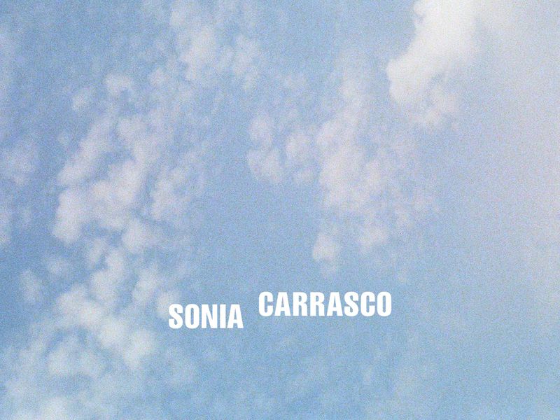 White bold typography reading 'SONIA CARRASCO' set against a bright blue sky with soft white clouds.