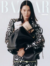 Model Haojie Qi holding an oversized black leather tote bag filled with newspapers in a patterned jacket against a white background.