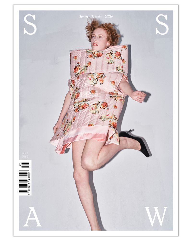 Model jumping in mid-air wearing a structured floral quilted pink dress and black high heels on a magazine cover.