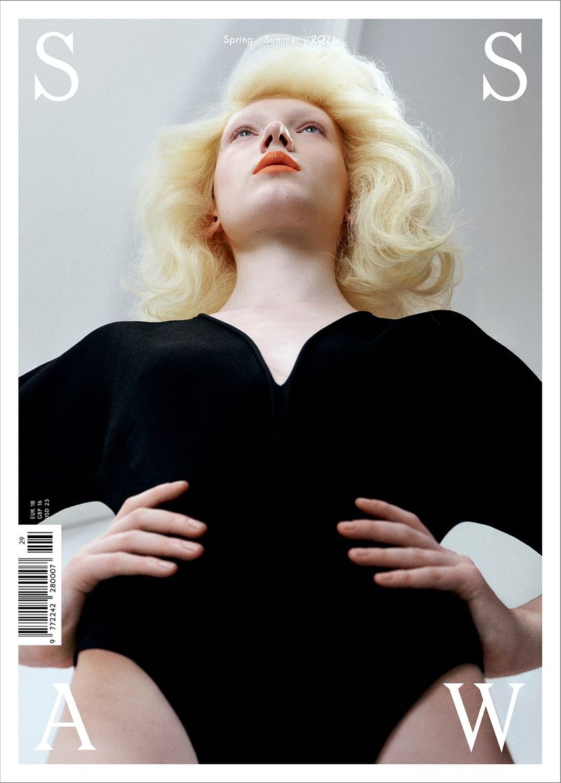 Low angle view of a blonde model with styled voluminous hair wearing a black bodysuit on a magazine cover.