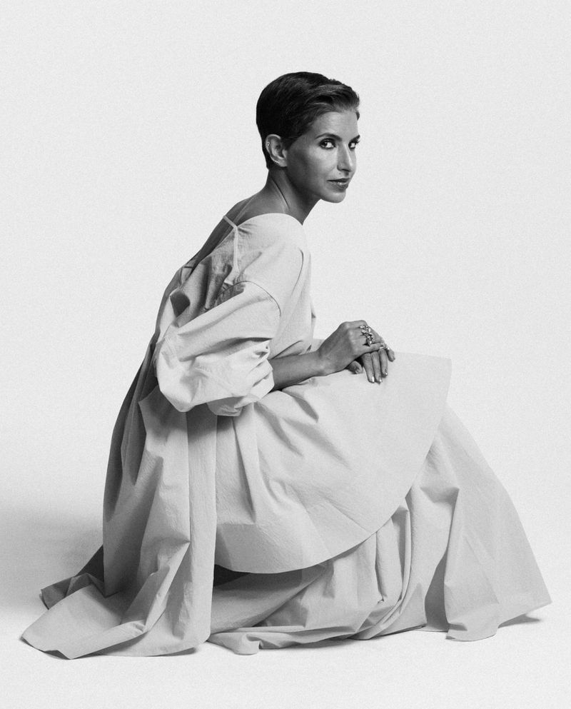 Deena Aljuhani Abdulaziz kneeling in a voluminous structured light gown against a seamless white studio backdrop.