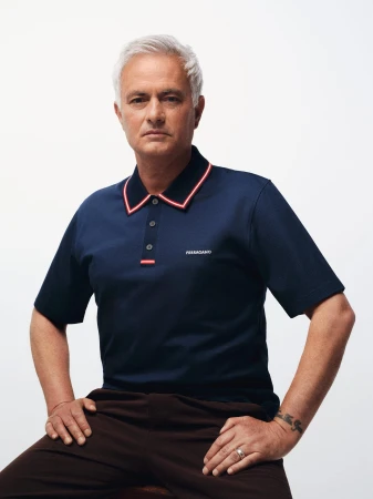 José Mourinho seated in a navy blue Ferragamo polo shirt with red collar trim against a white seamless background.