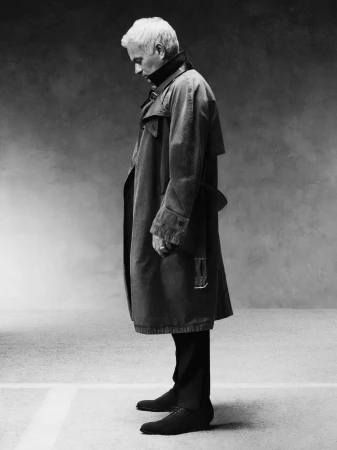 José Mourinho stands in profile wearing a long trench coat with a raised dark collar in a monochrome studio portrait.